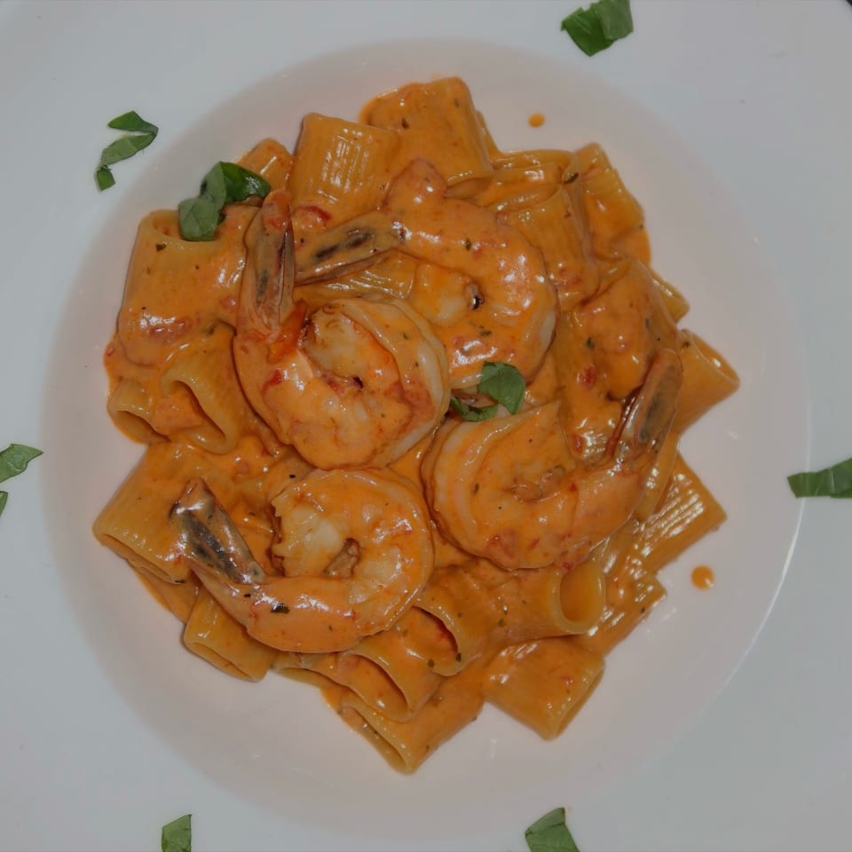Rigatoni pasta with shrimp in creamy tomato sauce, garnished with fresh basil on a white plate.