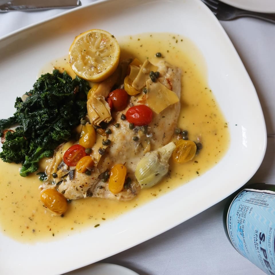 Chicken piccata with lemon, capers, artichokes, tomatoes, and sautéed spinach in a buttery sauce.
